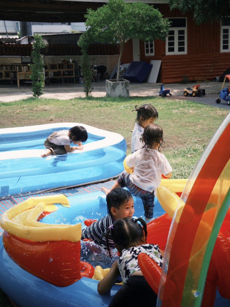 Children splashing in a pool during a swimming lesson at Firefly Forest School in Bangkok.

